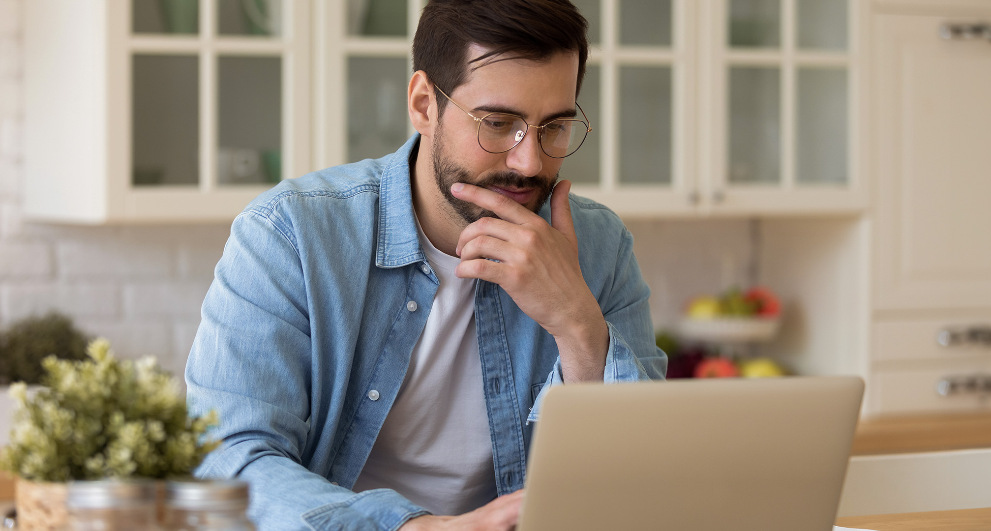 osoba s naočalama sjedi u kuhinji i gleda u laptop